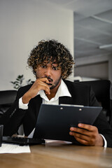 An indian businessman is sitting at a desk in the office and attentively checking work documents.