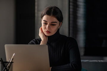 Portrait of young beautiful brunette business lady focused looking at laptop screen while sitting at desk in home office.