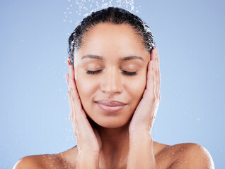 Face, natural and shower with woman in studio isolated on blue background for skincare. Beauty, hydration and wet with aesthetic model washing in water drops for dermatology, hygiene or wellness