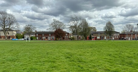 Obraz premium A well-maintained grassy field stretches towards a row of red-brick houses, featuring goal posts for football games, located near Gain Lane in Bradford, UK.