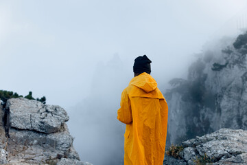 A solitary figure in a vibrant yellow raincoat conquers the majestic mountain peak, shrouded in...