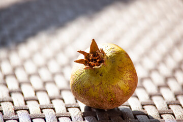 An unripe green pomegranate on a wicker brown table in the sunlight. An autumn fruit. Healthy food. Horizontal