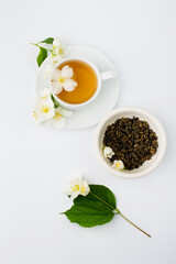 Cup with green tea and jasmine flowers on a white background, top view.