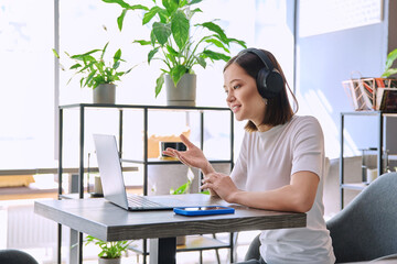 Young woman in headphones having video chat conference using laptop sitting in cafe