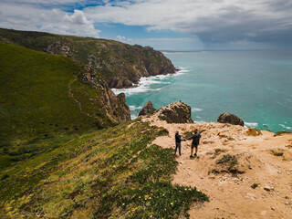 Cabo da Roca is the westernmost cape of the Eurasian continent, located in Portugal. A couple walking on a rocky ocean shore.