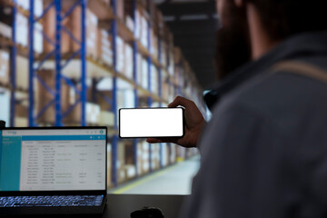 Storehouse employee looking at phone with blank display template, verifying industrial stock labels...