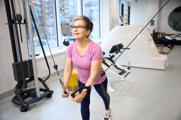 Fototapeta premium Middle aged caucasian woman doing sport exercise for chest muscles in gym