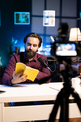 Experienced voice actor in studio working on audiobook recording production, reading from book,...