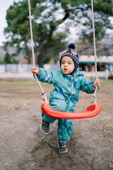 Little girl is standing, leaning her knee on a rope swing