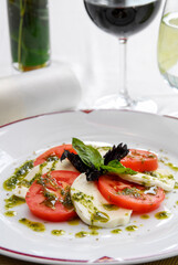 caprese salad with ripe tomatoes and mozzarella cheese with fresh basil leaves and dressing on restaurant table