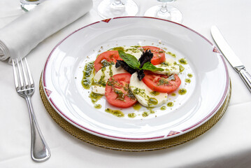caprese salad with ripe tomatoes and mozzarella cheese with fresh basil leaves and dressing on restaurant table