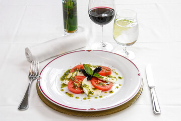 caprese salad with ripe tomatoes and mozzarella cheese with fresh basil leaves and dressing on restaurant table