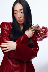 Beautiful Asian woman in red leather jacket holding a bouquet of flowers in urban setting