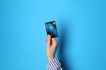 Woman holding credit card on light blue background, closeup