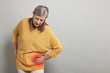 Senior woman suffering from pain in hip on grey background. Space for text