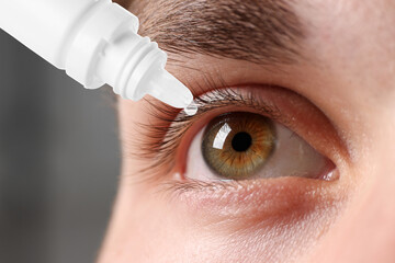 Man applying eye drops on grey background, closeup