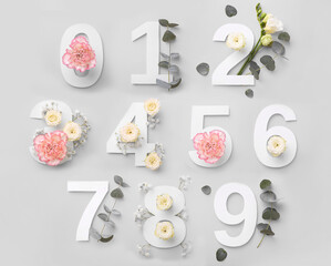 Numbers and beautiful flowers on light grey background, top view
