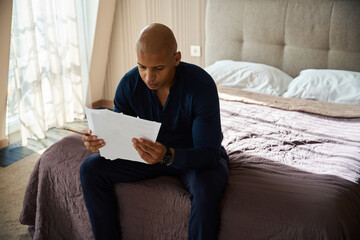 Focused african american entrepreneur watching documents on bed in hotel room
