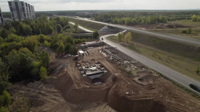 Process of building road hotel near highway with lively traffic. Construction site placed on way out of town with workers and materials