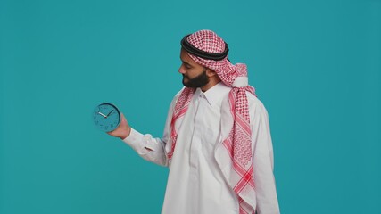 Middle eastern man checks wall clock to look at time, using timepiece to see hour and minutes....