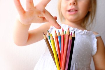 small child, blonde girl holds joyfully a bunch of colored pencils, counts them, concept of parenting, student writing supplies, back to school, names colors, drawing, learning to draw