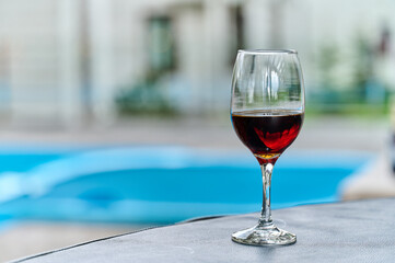 A glass of wine is on a round table on the background of the pool.