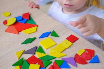 child, toddler, girl plays with colored wooden geometric figures, cubes, builds houses and animals,...