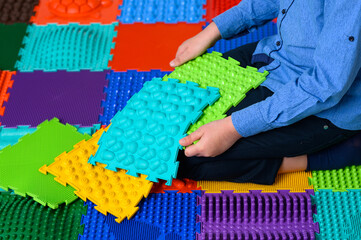 A boy sits on an orthopedic mat and collects it