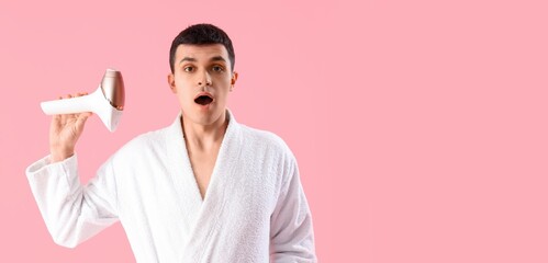 Surprised young man holding photoepilator on pink background with space for text