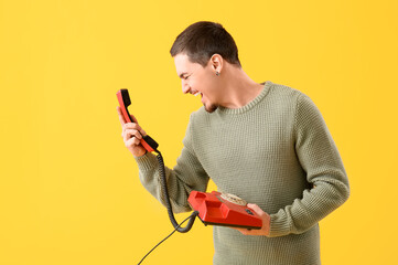 Angry young man with telephone on yellow background