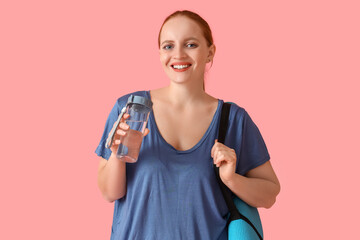 Portrait of sporty young woman with bottle of water and yoga mat on pink background