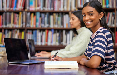 Portrait, university and woman in library with laptop, research and writing notes with bookshelf....