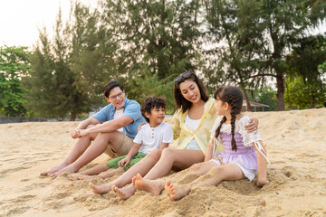 Fototapeta premium Happy Asian family travel at the sea on summer beach holiday vacation. Father, mother and child kids enjoy and fun outdoor lifestyle walking and playing together on tropical island beach at sunset.