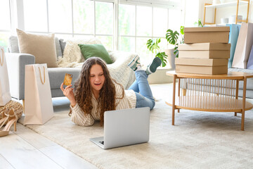Young woman with credit card, laptop, bags and boxes shopping online at home - Powered by Adobe
