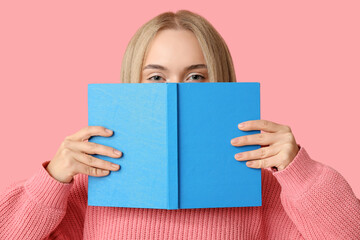 Beautiful happy young woman with book on pink background