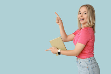 Beautiful young happy woman with book pointing at something on blue background