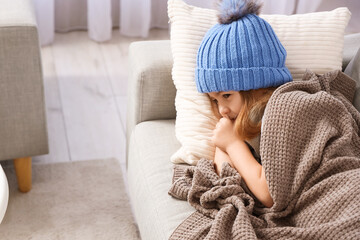 Sick little girl in hat coughing on sofa at home