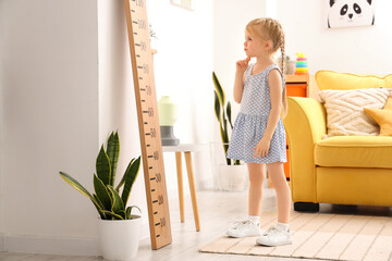 Thoughtful little girl near wooden stadiometer at home