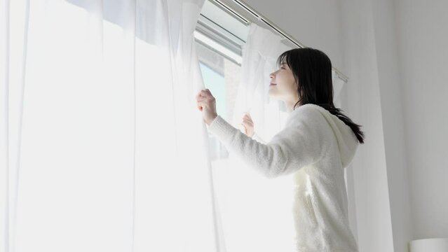 朝、カーテンを開ける女性