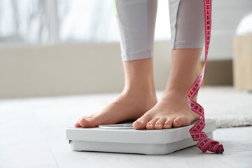 Young woman with measuring tape standing on scales at home. Diet concept