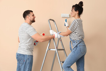 Beautiful young couple with paint rollers near beige wall doing repair in new house