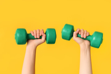 Female hands with green dumbbells on yellow background, closeup