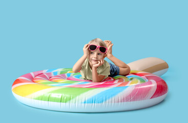 Cute little boy lying on swim mattress against blue background