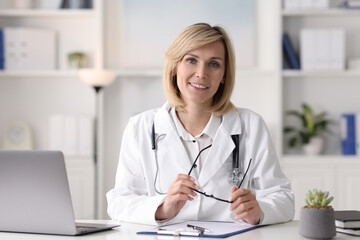 Smiling doctor with laptop having online consultation at table in office