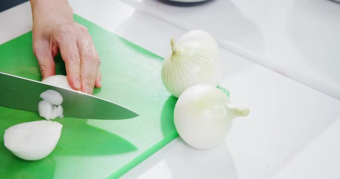 Woman's hands cutting onion on a professional kitchen board.