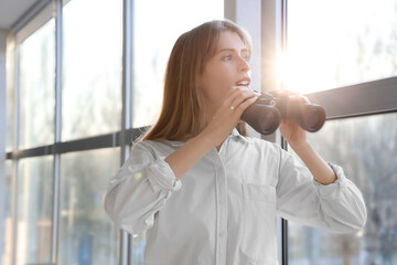 Young woman with binoculars looking in window at home