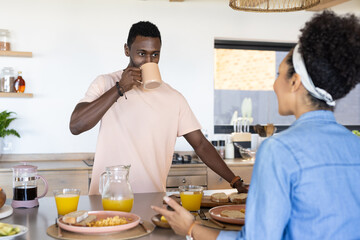 A diverse couple enjoying breakfast at home, with sunny background