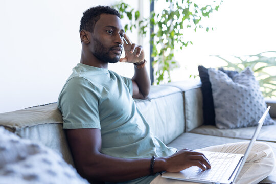 An African American man at home, wearing light blue shirt, using a laptop