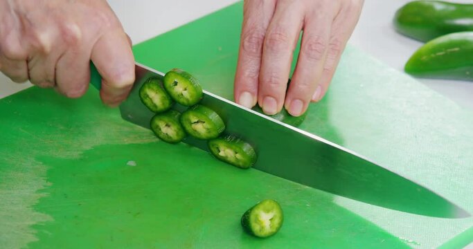 Close-up shot of hands cutting jalapeno pepper on a green kitchen board.