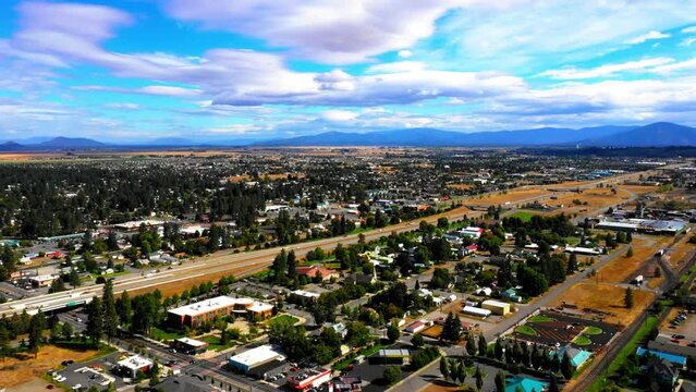 Aerial Scenic View Of Buildings Amidst Green Trees Under Cloudy Sky, Drone Flying Backwards On Sunny Day - Coeur d'Alene, Idaho